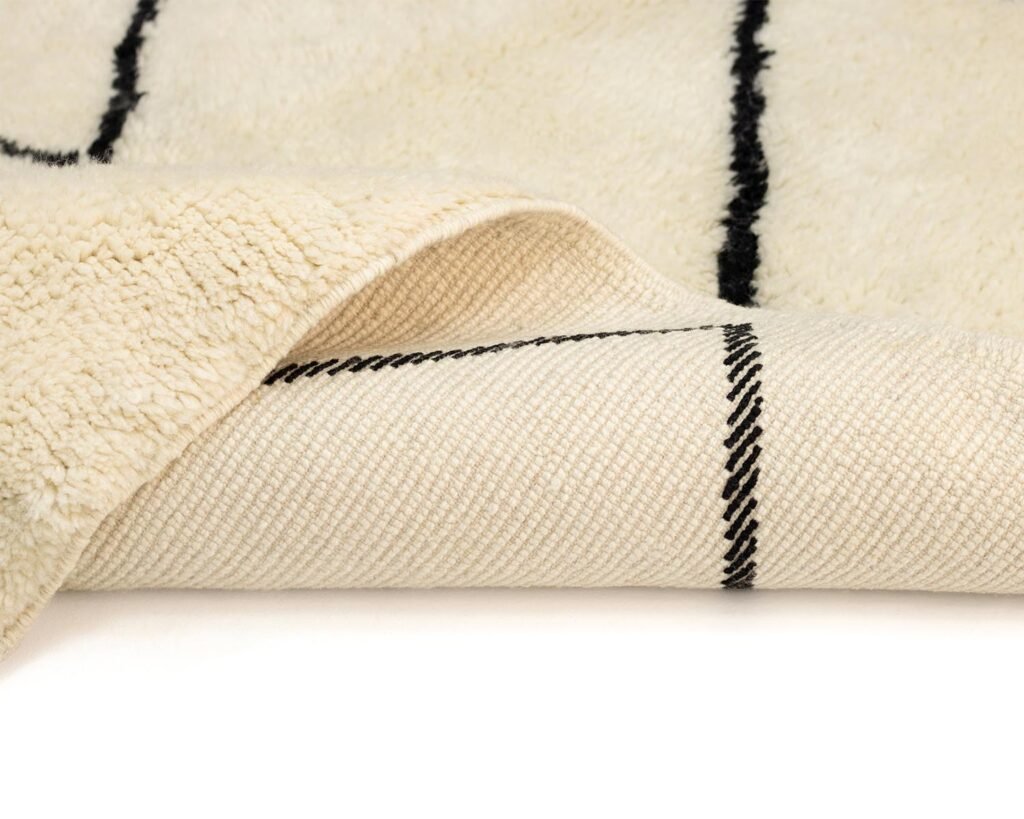 A close-up of a hand-knotted beige rug with a black grid pattern, showcasing a textured design. The underside reveals a finer weave of the same elegant pattern.