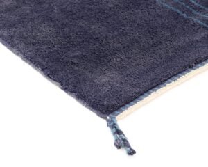 Close-up of a dark blue textured rug with fringe tassels on the corner, placed on a white background.