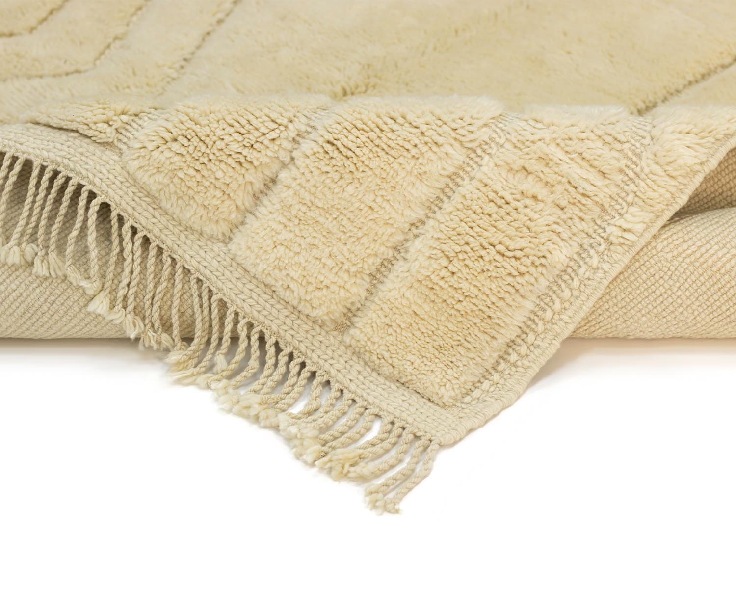 Close-up of a hand-knotted beige rug with a textured, thick, fluffy surface and fringe edging.