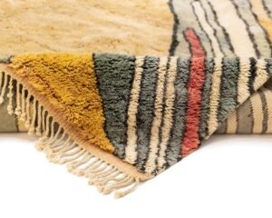 A folded, multicolored rug with fringe, displaying abstract patterns in green, yellow, red, and beige.