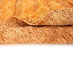 Close-up of a folded rug with a textured orange surface and a visible fluffy underside, displayed on a white background.