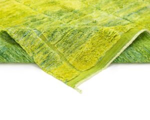 A green, textured blanket with a checkered pattern is partially folded over on a white surface, exuding the elegance reminiscent of luxury rugs.