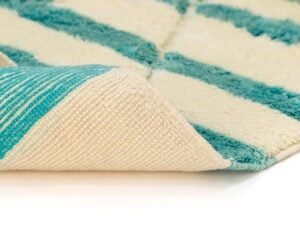 A rug with a turquoise and white striped pattern is shown close-up with a corner folded back, revealing the underside texture.