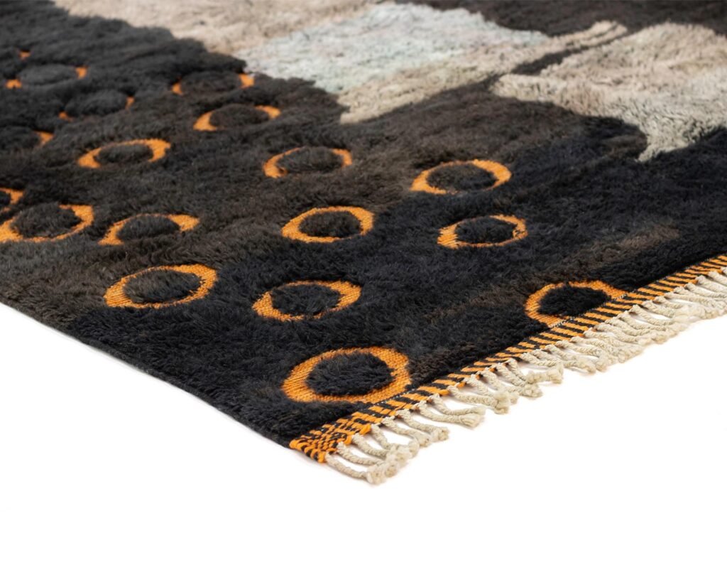 Close-up of a textured rug with orange circles on a dark background, featuring fringed edges.