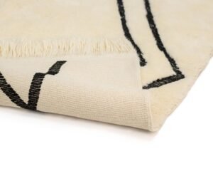 A beige rug with black abstract lines and fringed edges, elegantly folded at the corner.