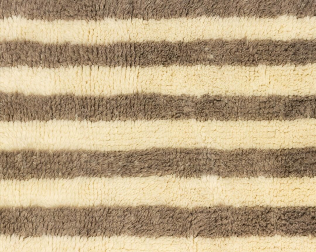 A close-up of a striped, textured fabric with alternating light cream and brownish-gray horizontal patterns.