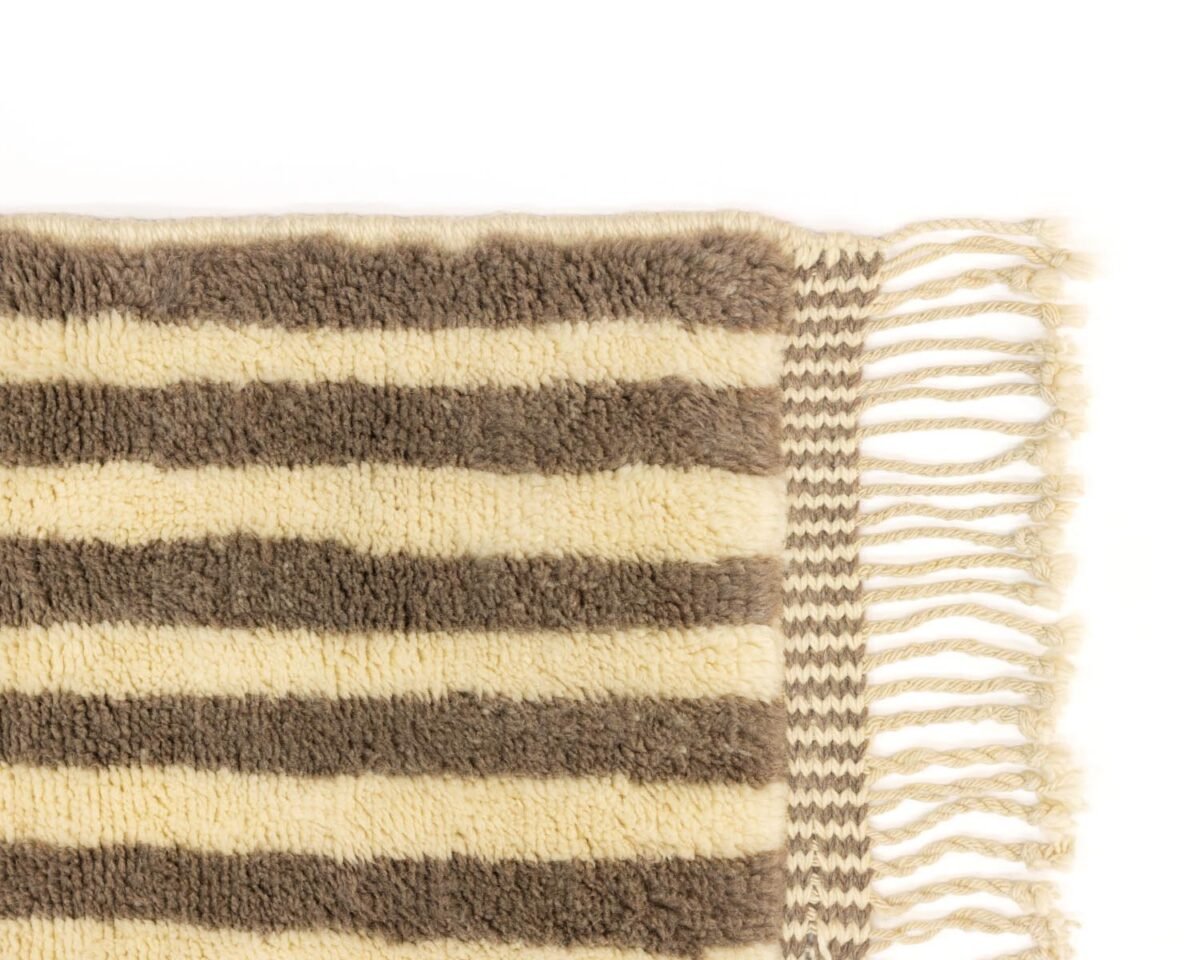 A detailed view of a striped wool rug showcases its alternating beige and brown patterns, accented by tassels adorning the right edge.