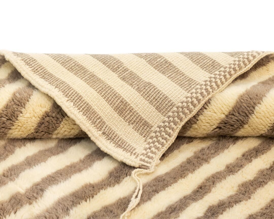 A folded, striped beige and brown throw features a woven edge with a soft, textured surface.