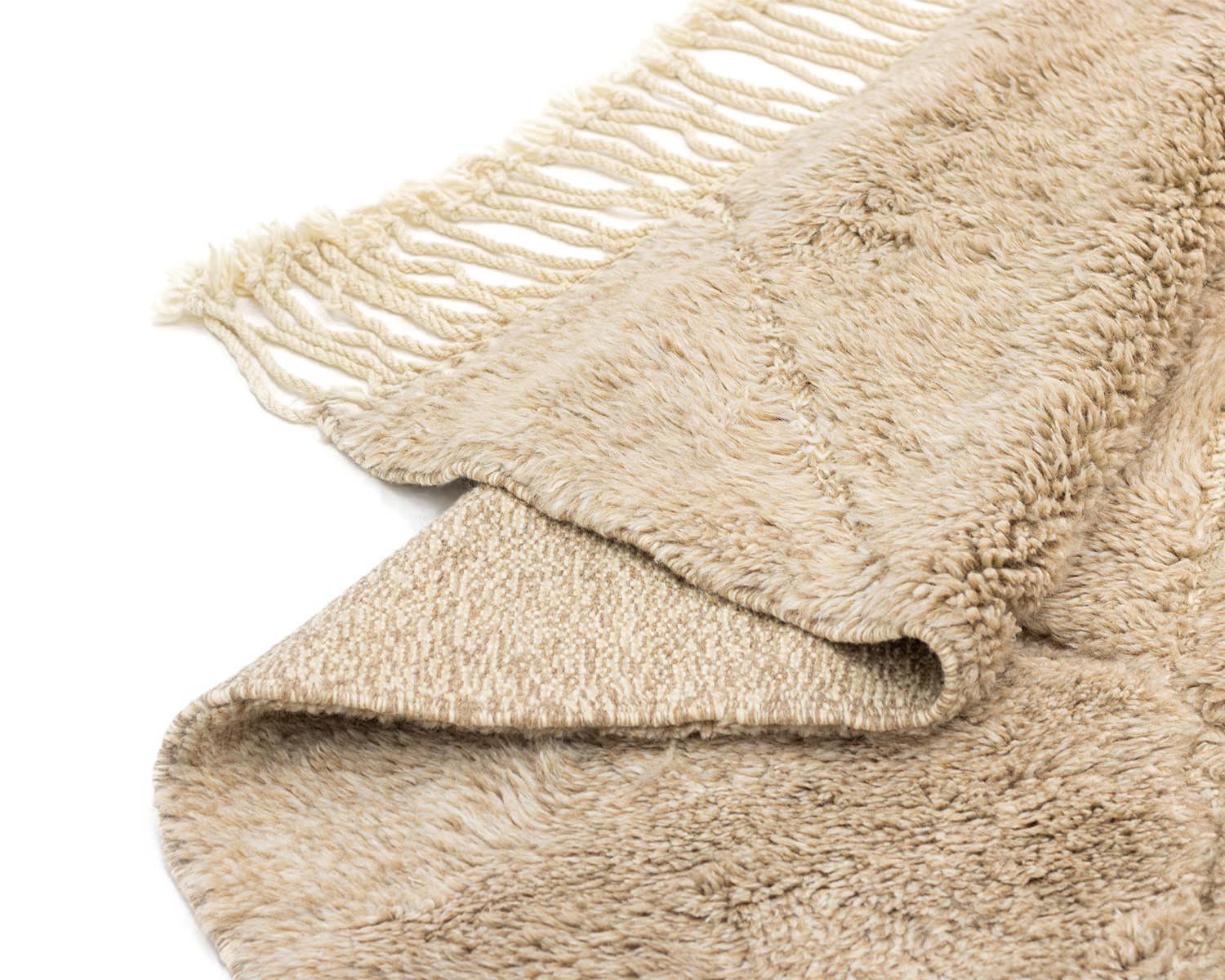 A luxurious fringe edge complements the intricate design of this beige textured piece, reminiscent of a hand-knotted Moroccan rug, set against a crisp white backdrop.