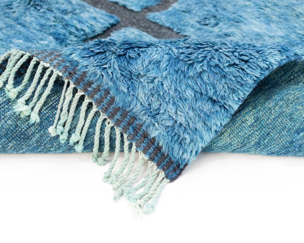 A blue, textured rug with fringed edges is gently folded over, showcasing its woven underside.
