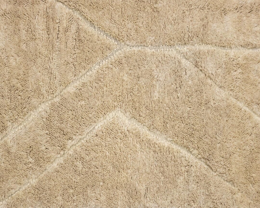 Close-up of a beige textured luxury rug with a subtle geometric pattern of intersecting lines and angles.