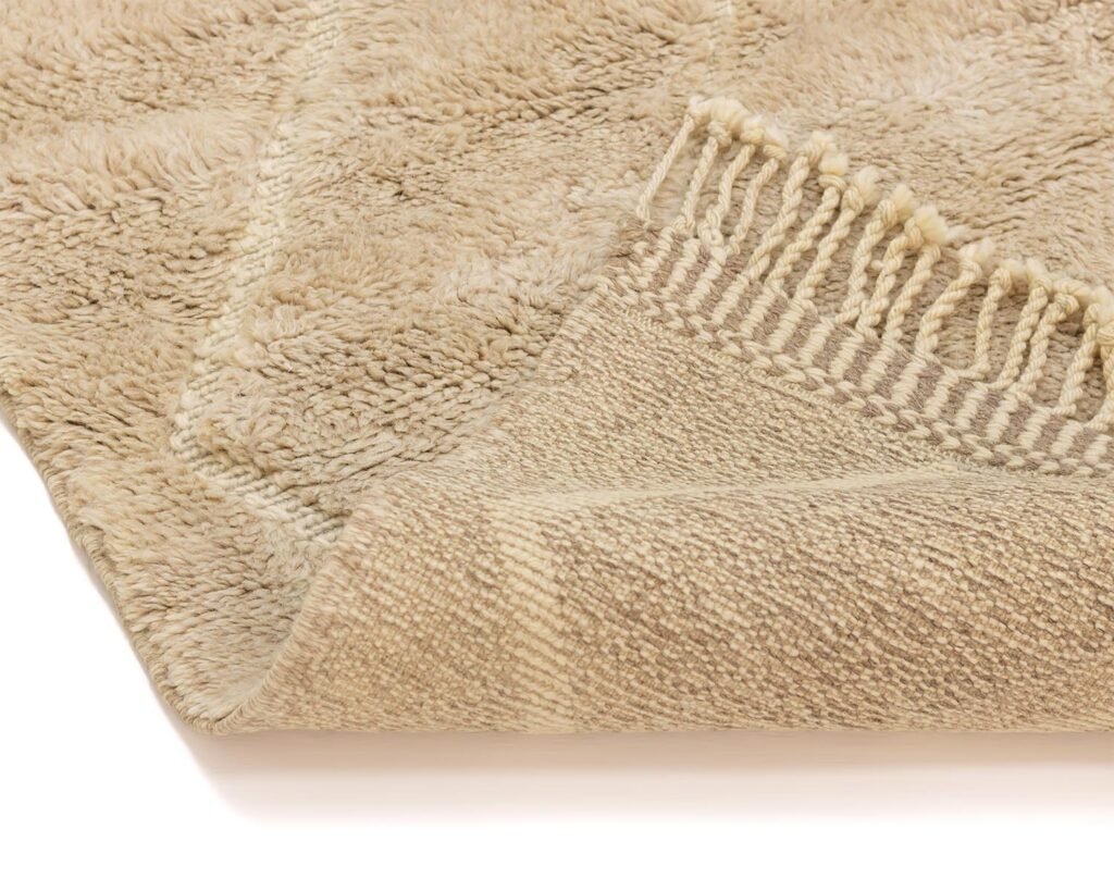 A beige, plush luxury rug with fringed edges elegantly folded over reveals its intricately woven underside.