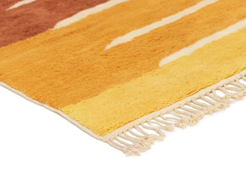 A corner of a woven rug with yellow and brown stripes and fringe on the edge is shown.