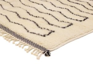 A cozy corner of a cream-colored rug featuring black zigzag patterns and delicate fringe on the edge.