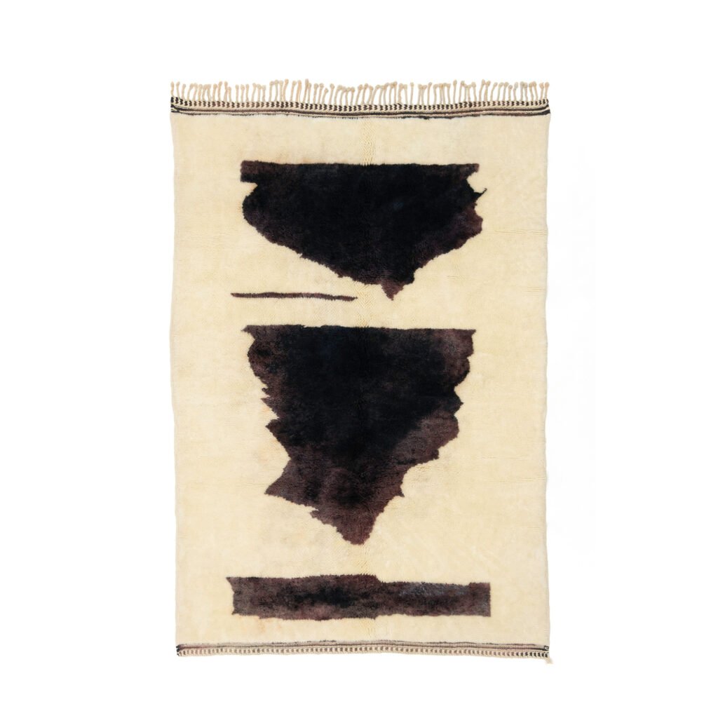 A beige rug with abstract black shapes in the center highlights three distinct dark areas and includes a chic, fringed edge on one side.