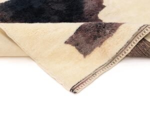 Close-up of a folded, tan and brown cowhide-patterned rug with a detailed border on a plain white background.