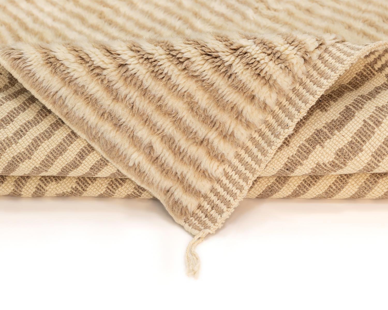 A soft, folded beige and brown striped luxury rug with a visible corner showcasing both sides of the pattern adds a touch of elegance to any space.