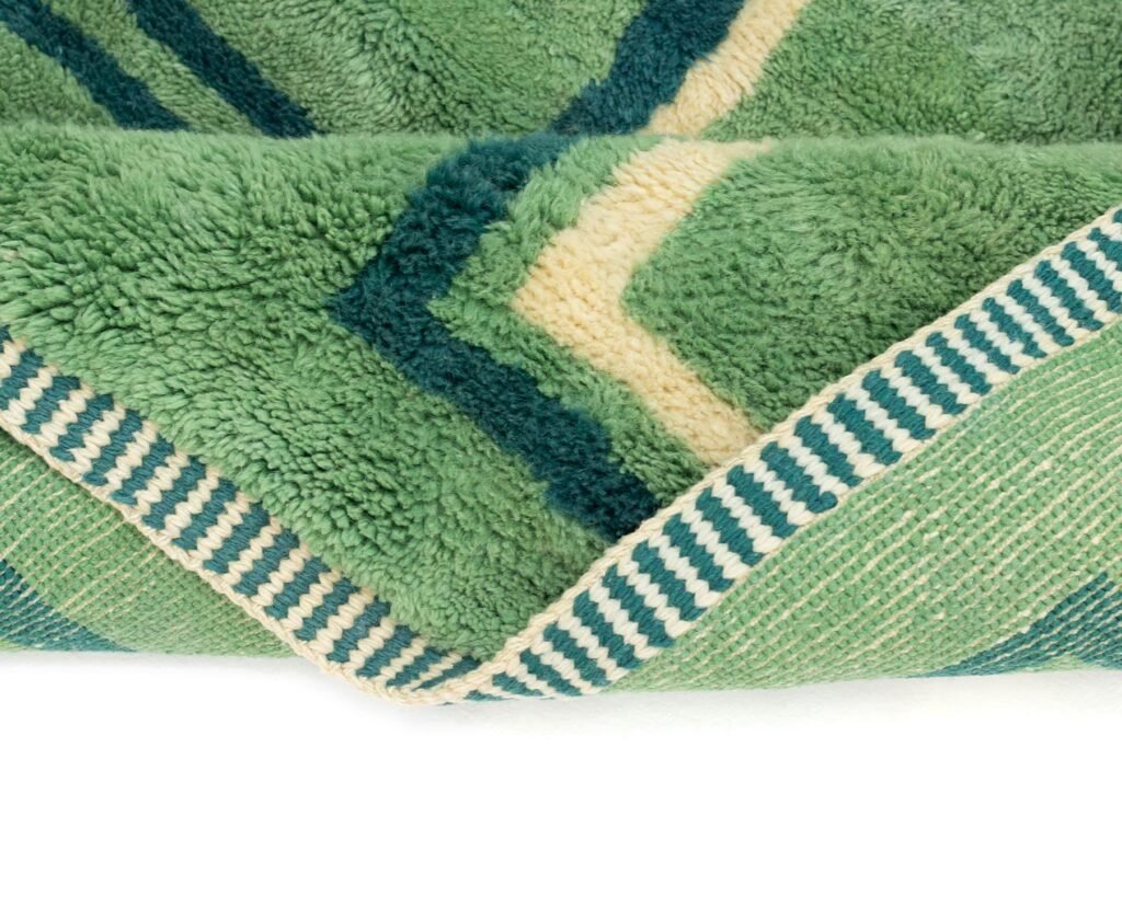 Close-up of a folded green rug with geometric patterns and a striped edge.