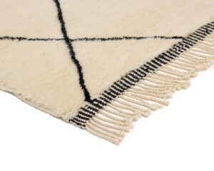 A cream-colored rug featuring a striking black crisscross pattern and fringed edges lies elegantly on the floor.