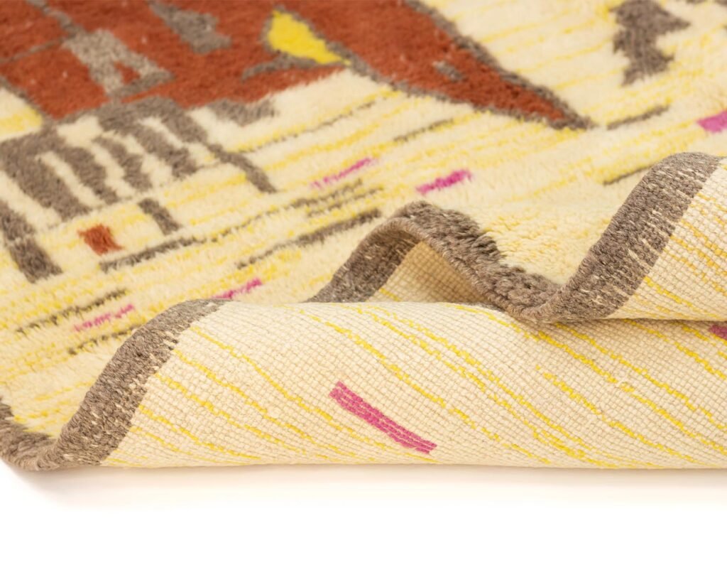 A luxury rug with abstract red, brown, and pink patterns is folded elegantly. Its hand-knotted texture showcases a woven appearance, complemented by gray borders.