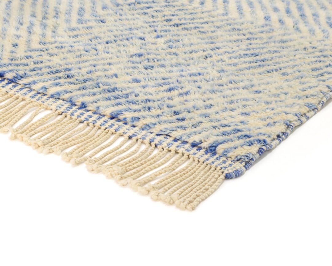 Close-up of a luxurious, hand-knotted rug showcasing blue and cream patterns with fringed edges.