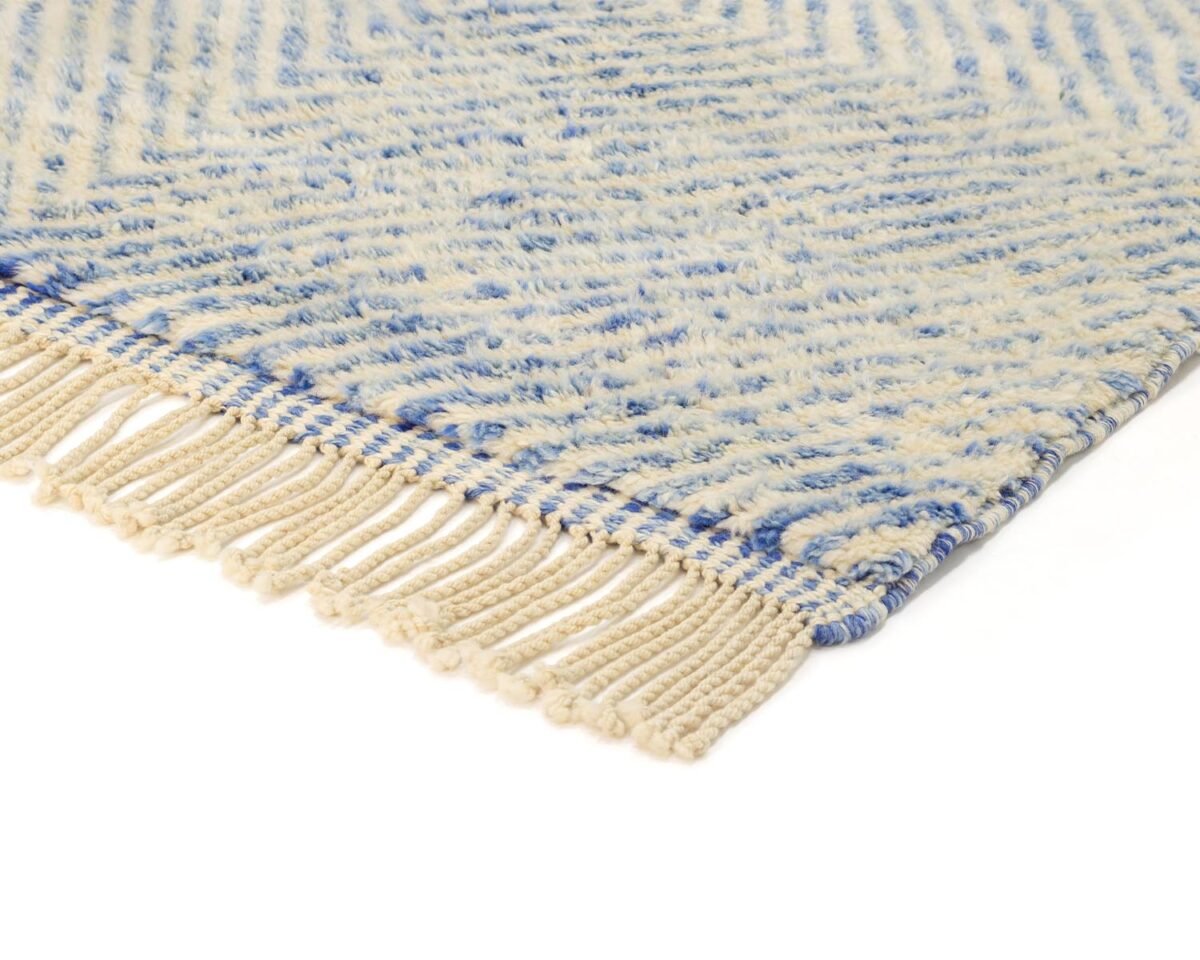 Close-up of a luxurious, hand-knotted rug showcasing blue and cream patterns with fringed edges.