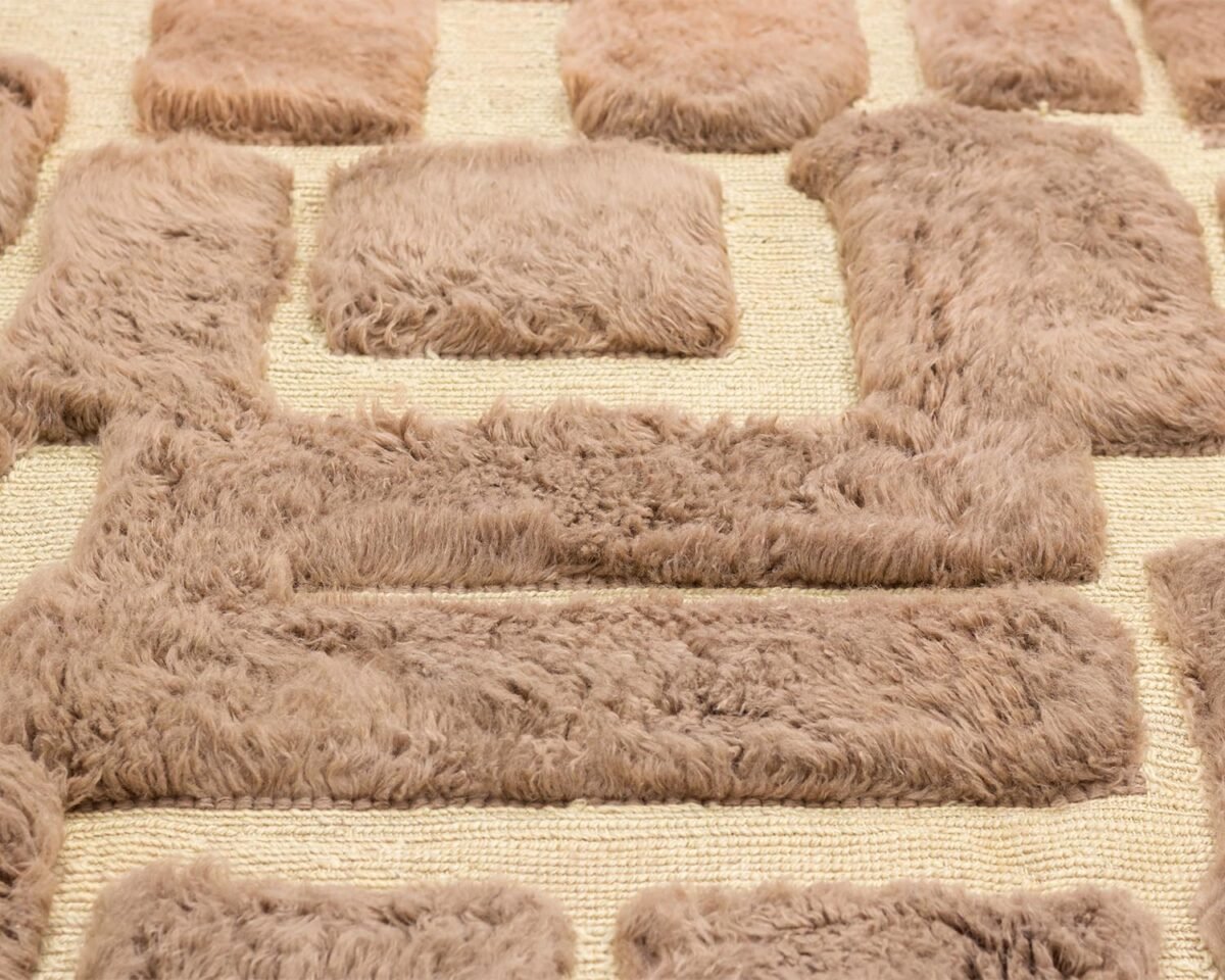 An authentic Moroccan rug showcases a close-up of its textured brown and beige design, with raised, fluffy rectangular patterns. This hand-knotted piece embodies artisanal craftsmanship, adding warmth and character to any space.