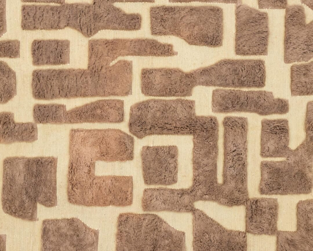 This hand-knotted, brown abstract geometric pattern graces a beige fabric background, featuring irregular shapes and varying textures.