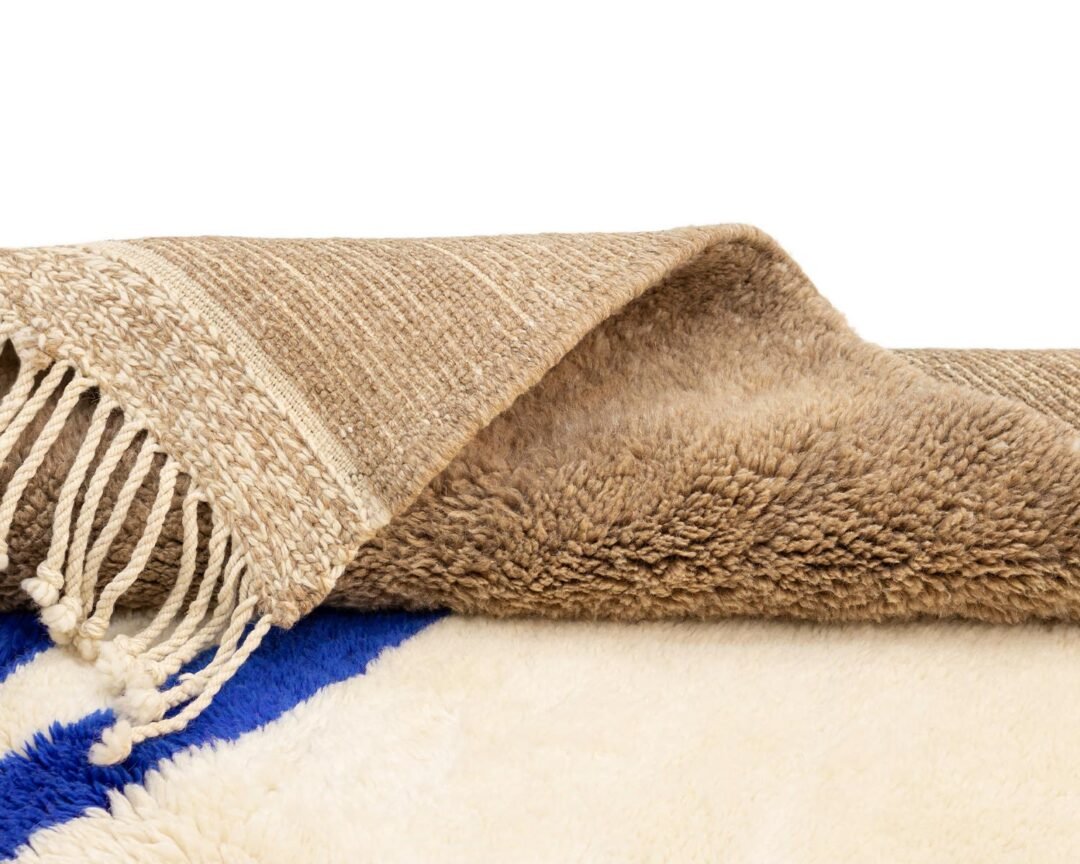 A luxurious beige and blue rug with tassels reveals its soft, fluffy underside.