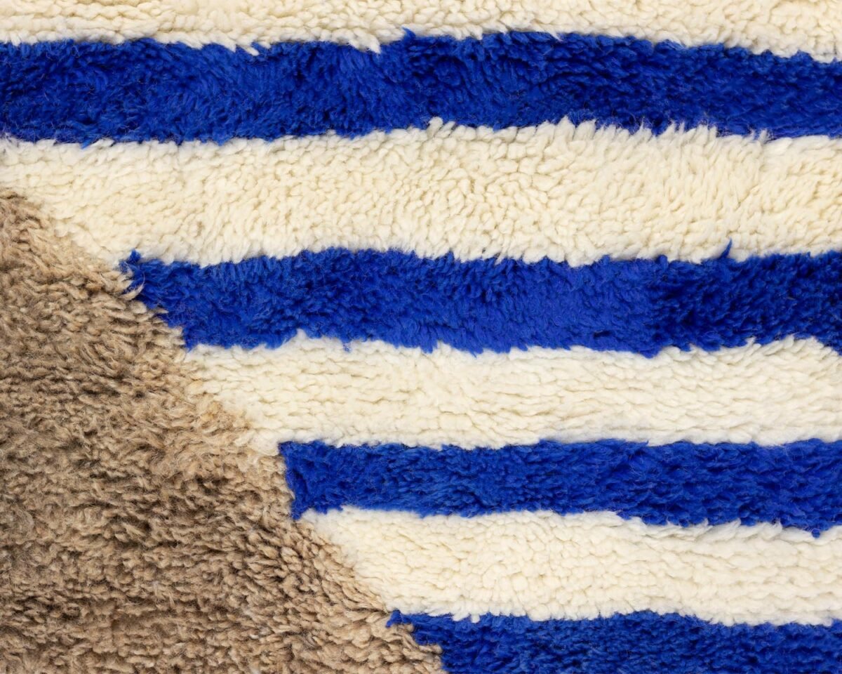 Close-up of a fabric featuring horizontal blue and white stripes, with a diagonal section of brown material at the bottom left, creating an intriguing pattern.