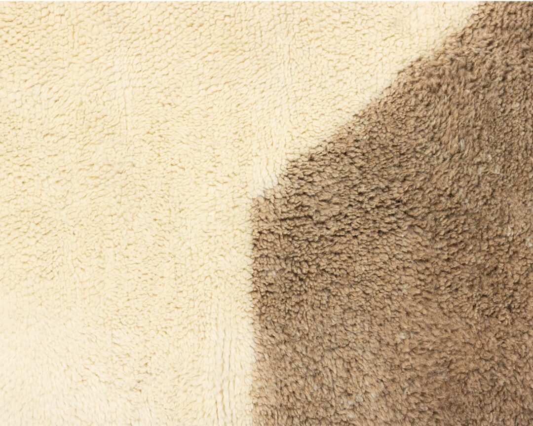 A close-up view reveals a soft and plush surface with two sections: one light cream and the other brown, resembling fleece or woolen textile.