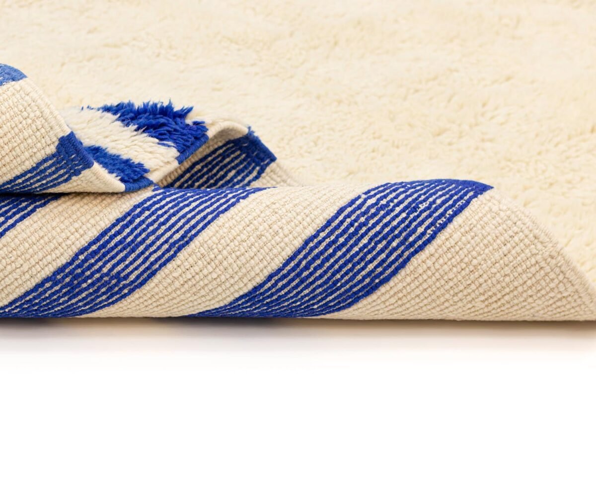 Close-up of a folded rug featuring bold blue and white diagonal stripes on a crisp white background.