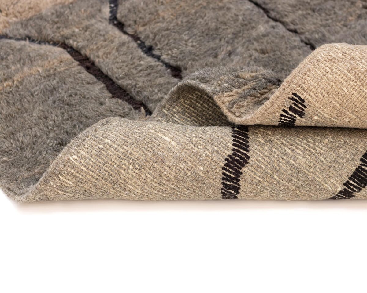 Close-up of a hand-knotted gray and beige wool rug featuring dark stripe patterns on a white background.