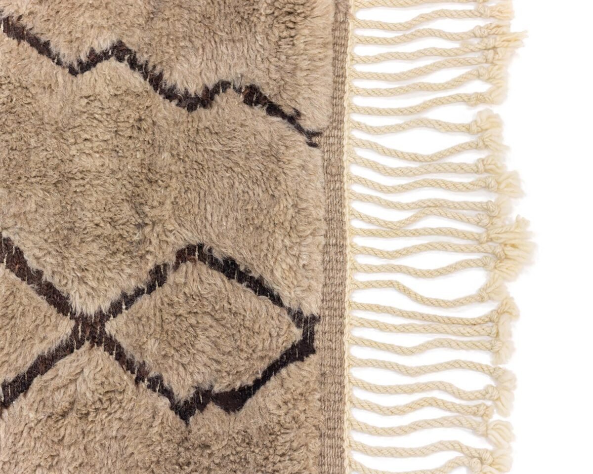 Close-up of an artisanal, hand-knotted beige and brown patterned rug with white fringes on the right edge.