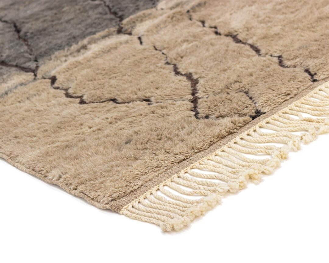 Close-up of an authentic Moroccan rug in beige and gray with black abstract lines. The hand-knotted rug features fringed edges on one side and a soft, shaggy appearance, showcasing its artisanal craftsmanship.