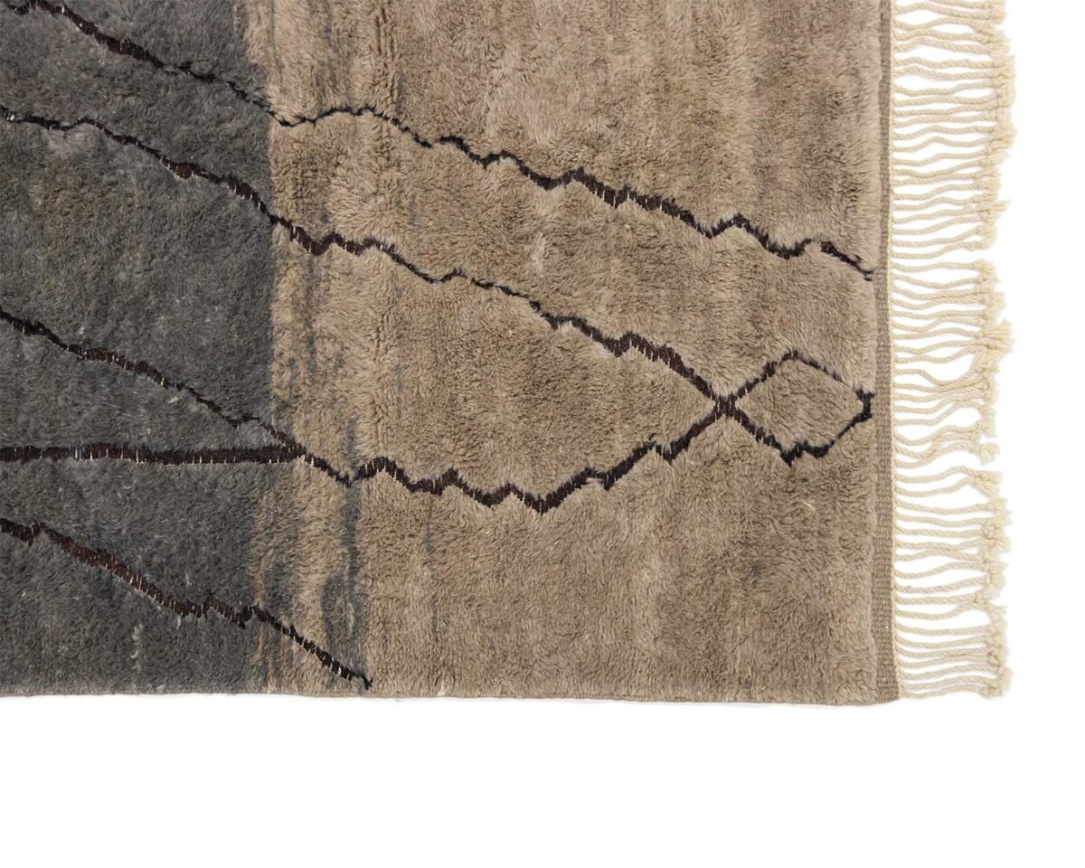 Close-up of an artisanal rug showcasing a wavy zigzag pattern and fringed edges on one side. The colors gracefully transition from dark gray to beige, adding a sophisticated touch to any room.