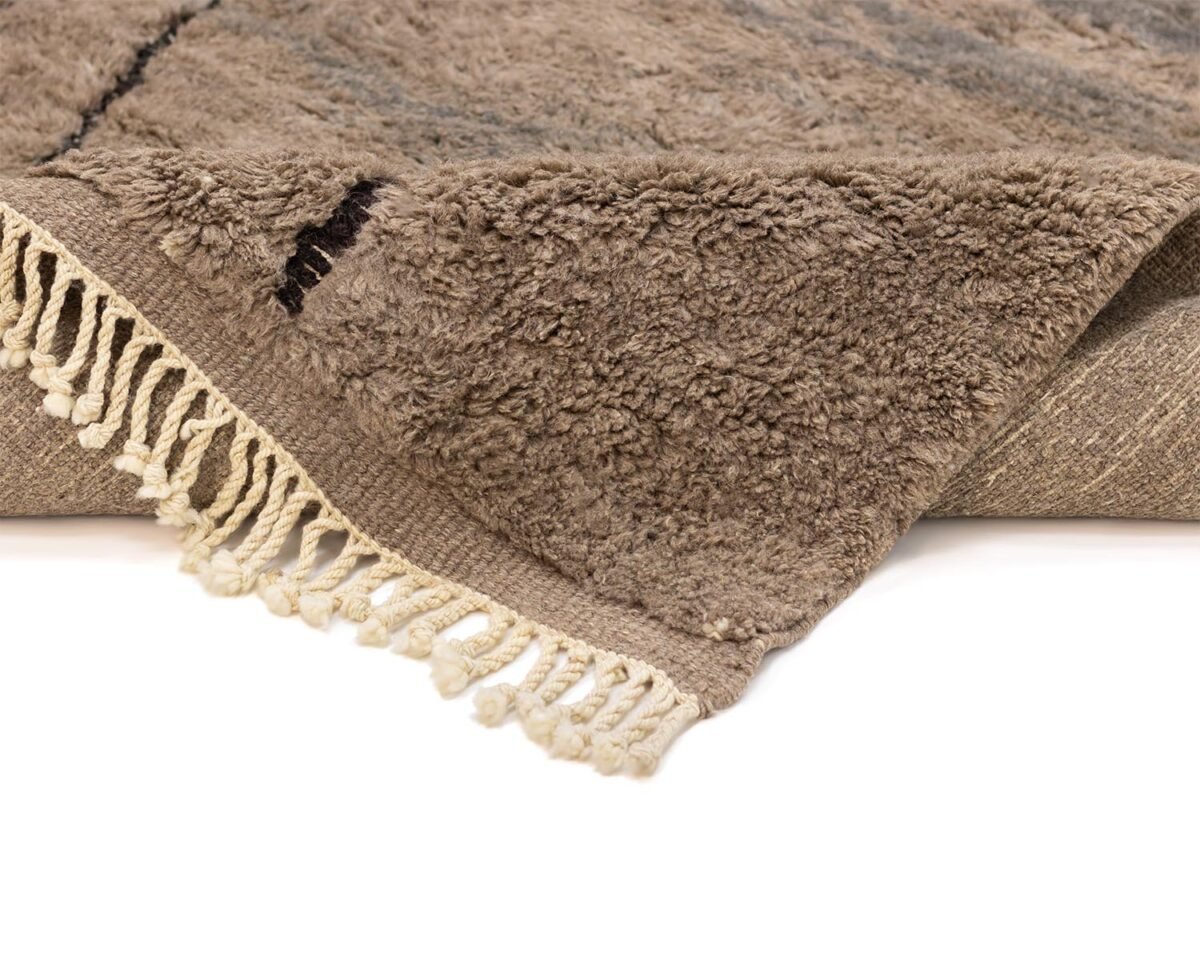 An artisanal rug with a soft, fluffy texture, this folded brown shag piece features ivory fringes on the edge. Perfect for adding warmth and style, its hand-knotted design showcases the craftsmanship of authentic Moroccan rugs.