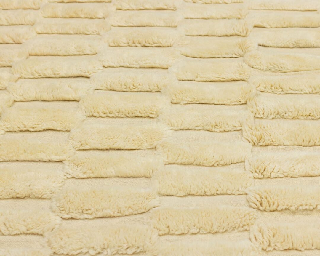 A detailed view of a textured surface showcasing parallel, rectangular, fluffy ridges in a soft cream hue.