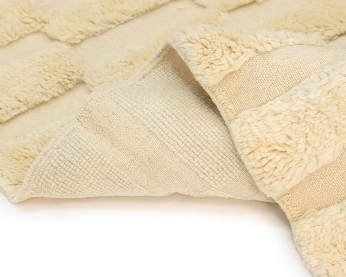 Close-up of a beige, textured rug with fluffy, raised sections and a smooth underside flipped over at the corner, exuding warmth and comfort.