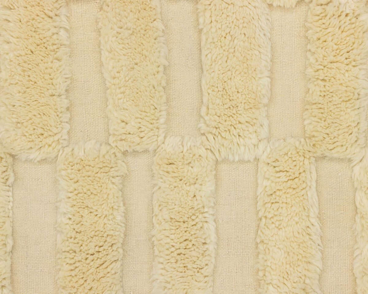 A close-up of a beige, textured fabric showcases parallel raised stripes of soft, fluffy material arranged vertically across the surface, evoking a cozy and inviting feel.