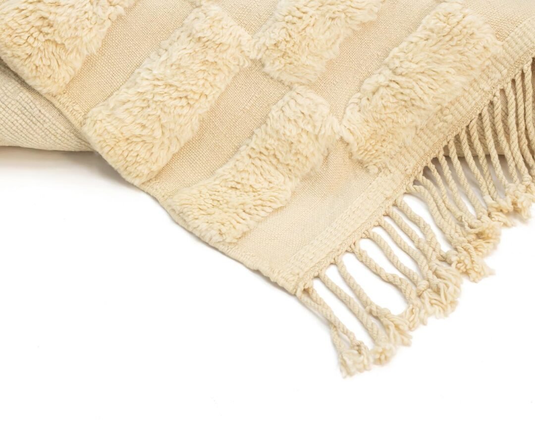 Close-up of a beige textured coverlet with fringe edges and raised rectangular patterns, exuding warmth and style.