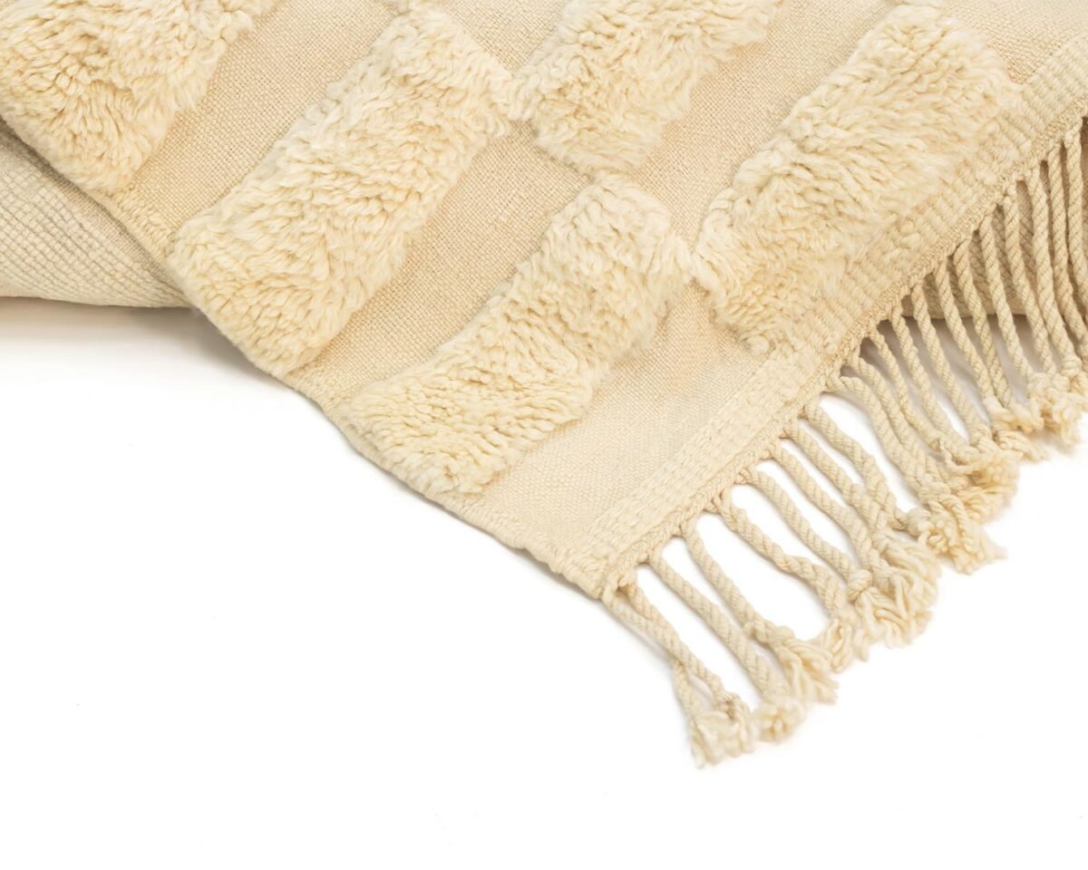 Close-up of a beige textured coverlet with fringe edges and raised rectangular patterns, exuding warmth and style.