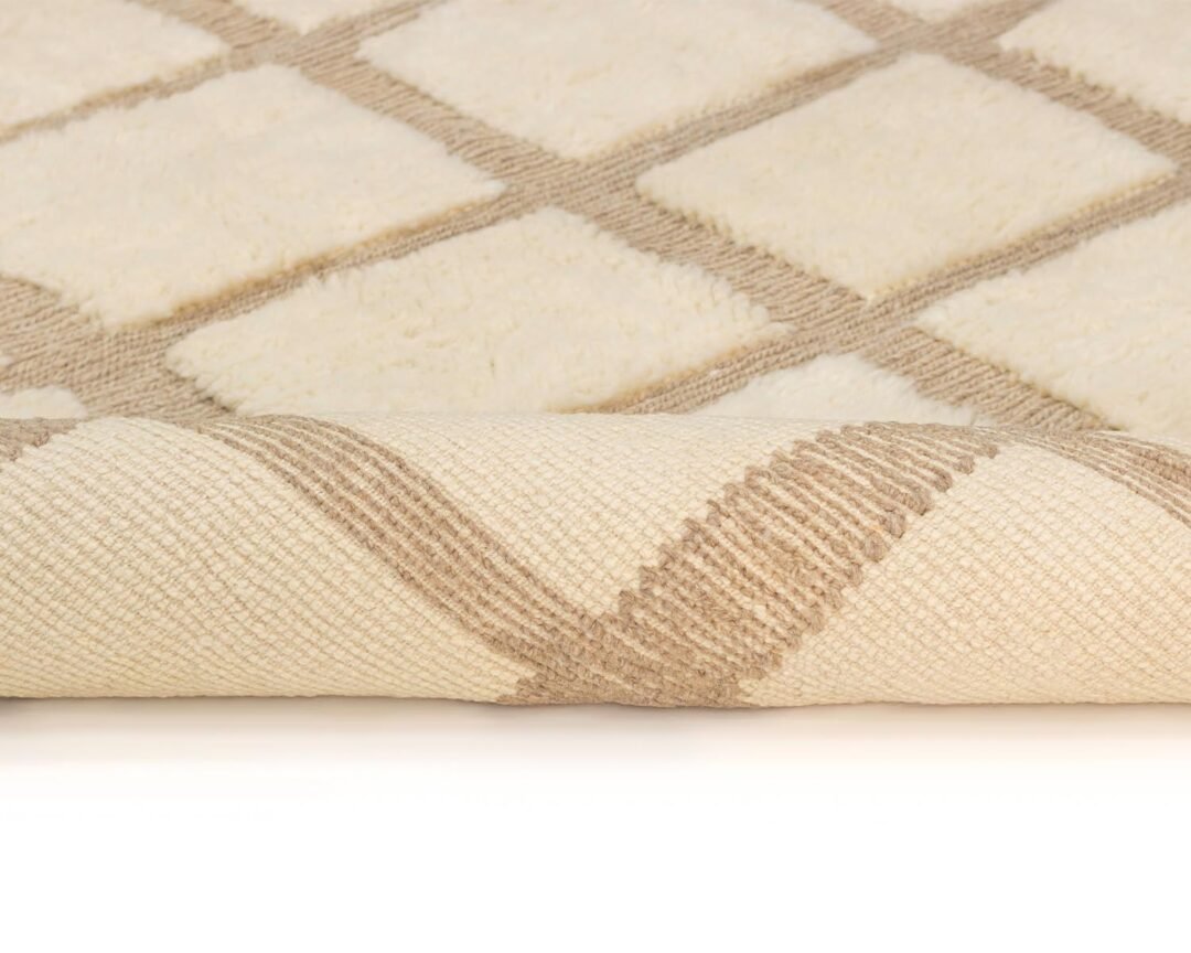 Close-up of a beige rug with a diamond pattern, rolled over at one end, showcasing its intricate woven texture.