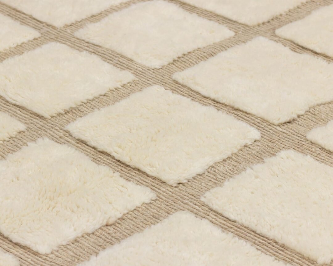 Close-up of a textured surface featuring a grid pattern with raised, soft, cream-colored squares on a beige background, reminiscent of plush upholstery.