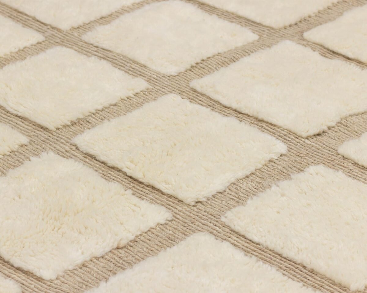 Close-up of a textured surface featuring a grid pattern with raised, soft, cream-colored squares on a beige background, reminiscent of plush upholstery.