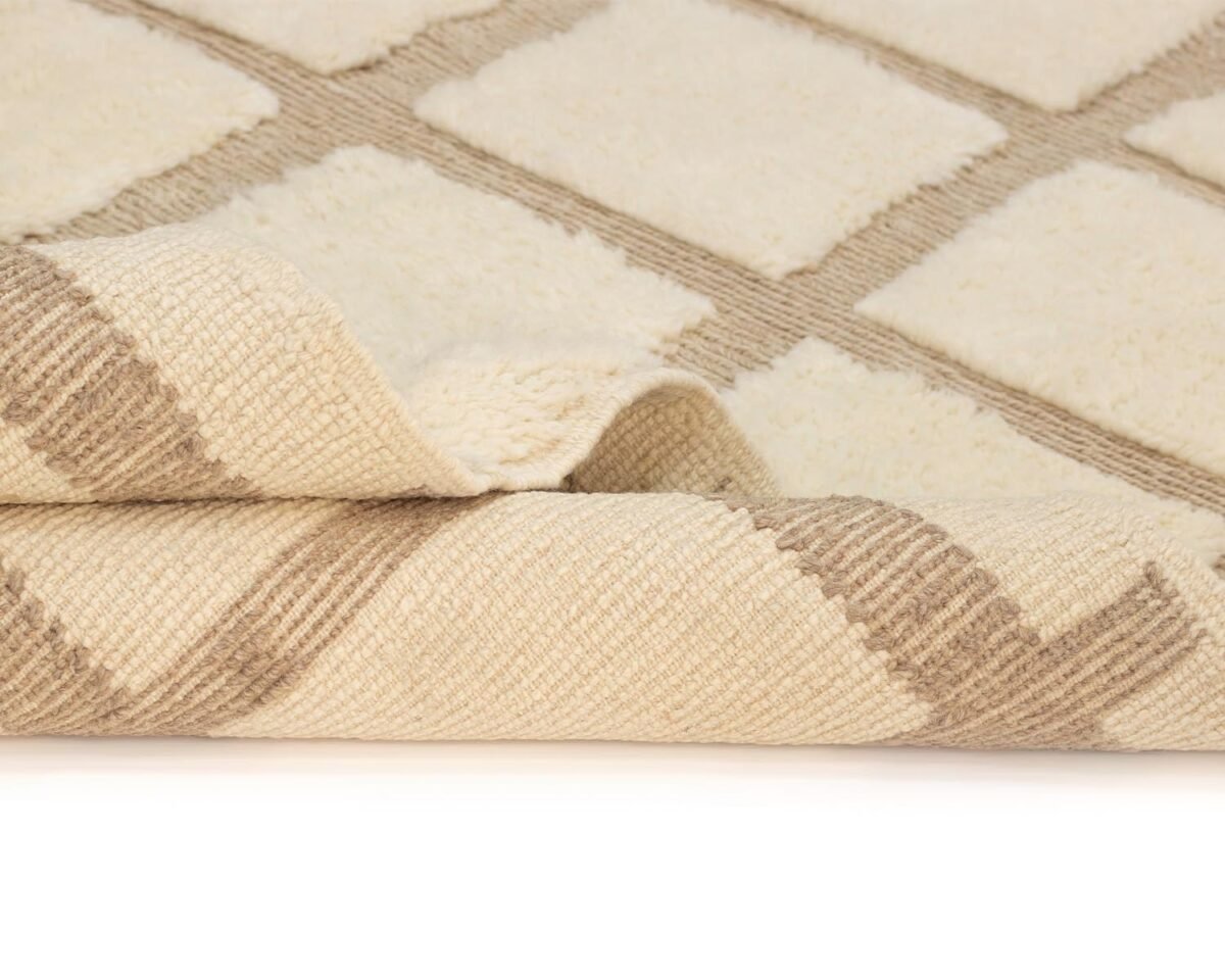 Close-up of a folded beige and cream woven rug featuring an intricate geometric pattern.