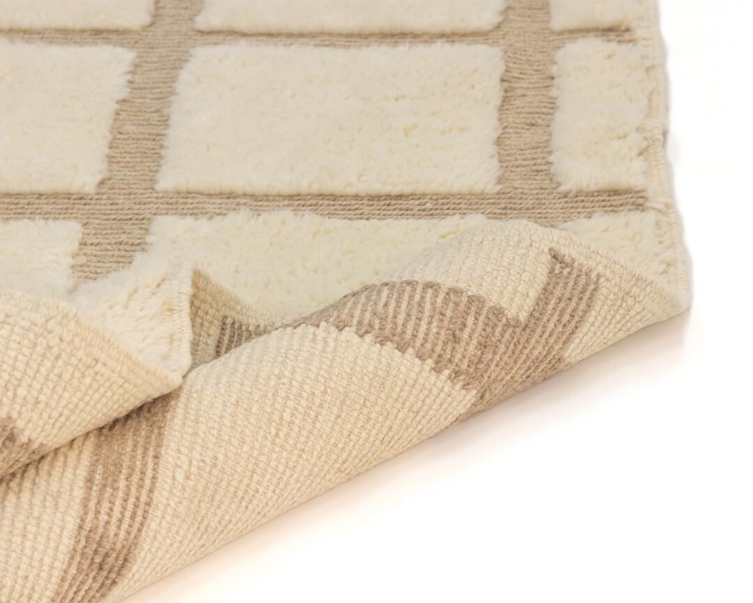 This close-up showcases a beige and cream textured rug with a captivating geometric pattern of squares. The corner is artfully folded, revealing its intricate underside.