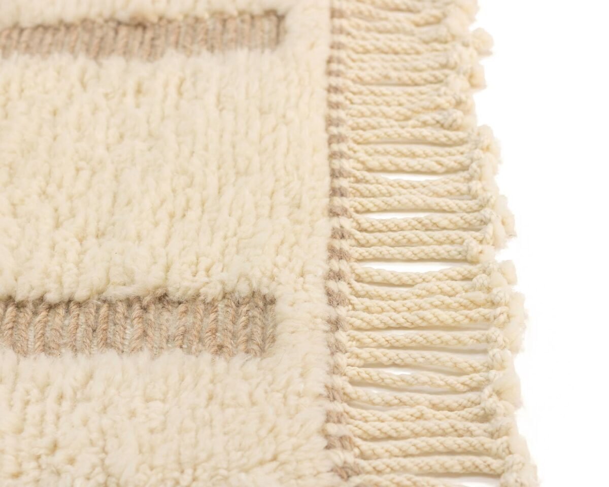 Close-up of a woven beige rug with tassels on the edge, featuring a pattern of rectangular shapes in earthy tones.