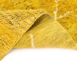A close-up of a yellow shaggy rug corner flipped over, revealing the woven underside with white geometric patterns.