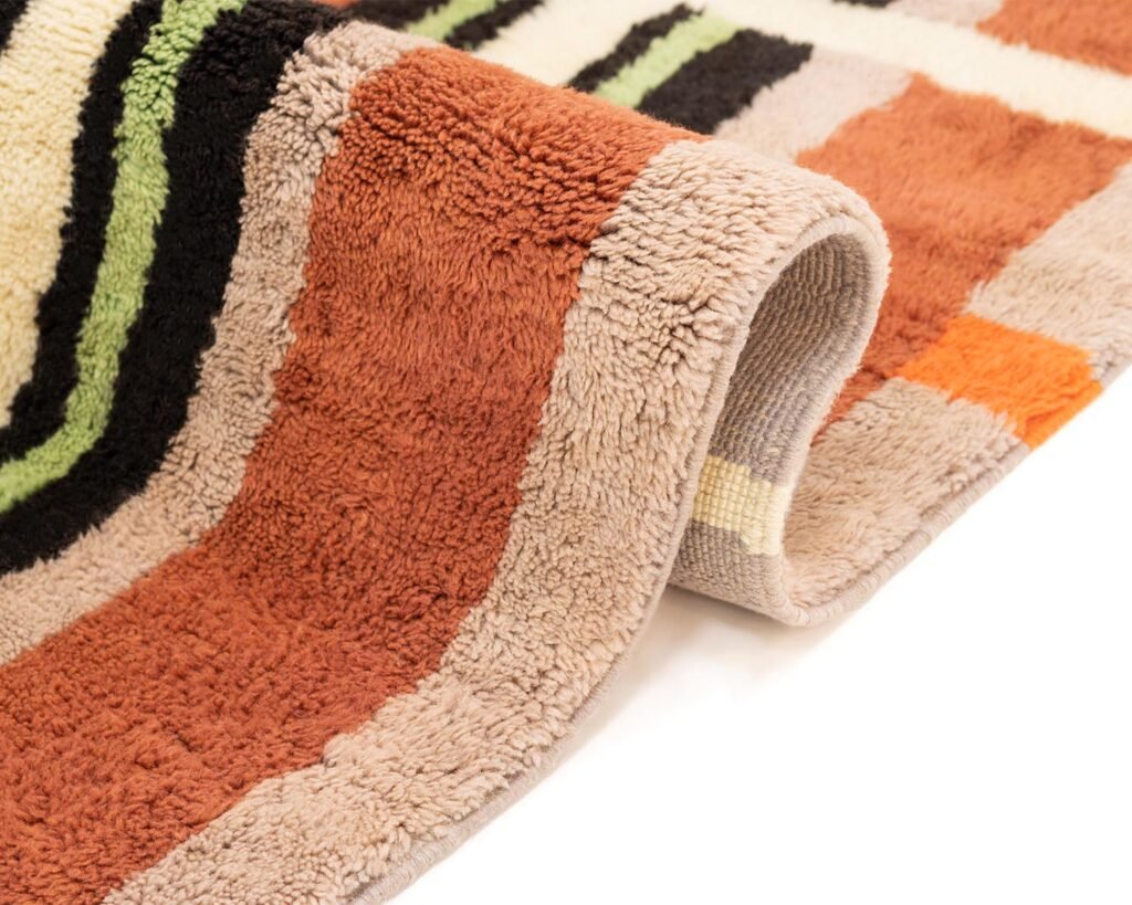 A close-up of a colorful, hand-knotted rug featuring brown, black, orange, and green stripes. This luxurious piece showcases a slight roll at the edge.